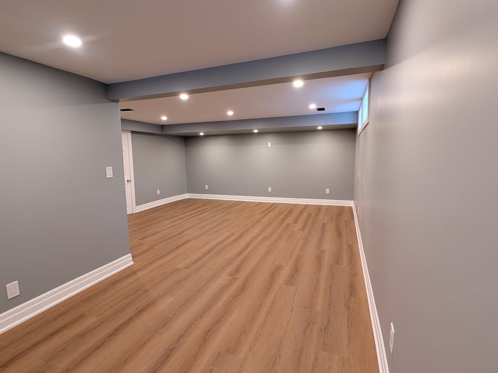 Finished basement living space with grey walls, wide-plank wood-look flooring, and recessed ceiling lighting