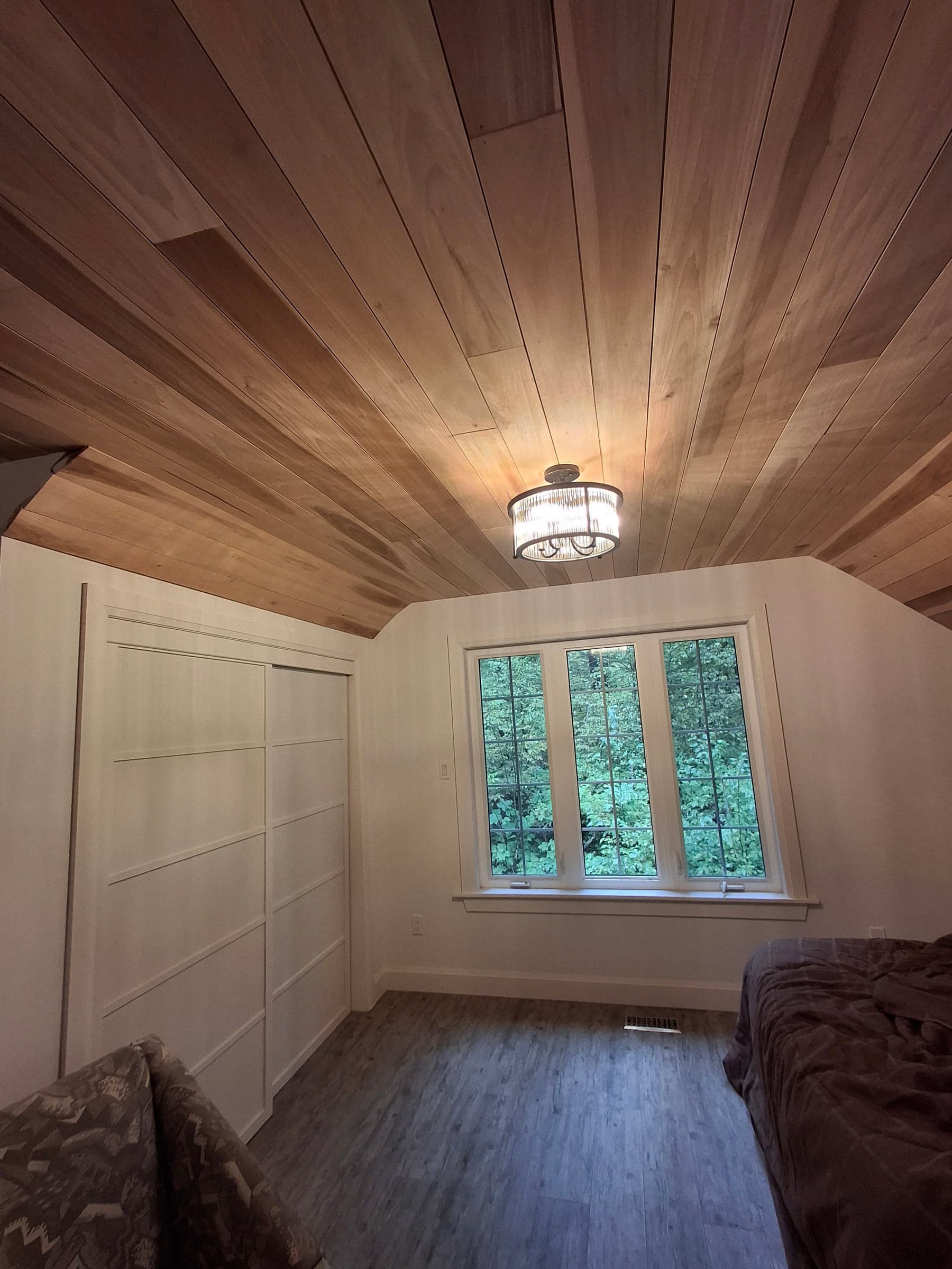 Converted attic room with a cedar ceiling, window, bed, and built-in storage