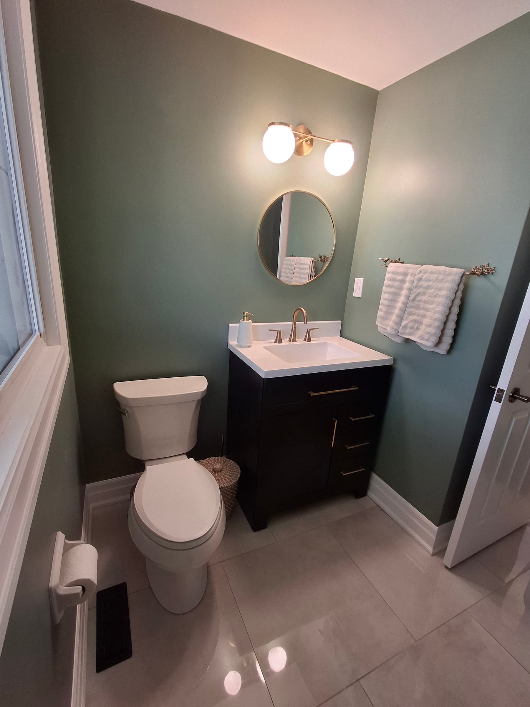 Compact powder room with green walls, a dark vanity, and brass fixtures