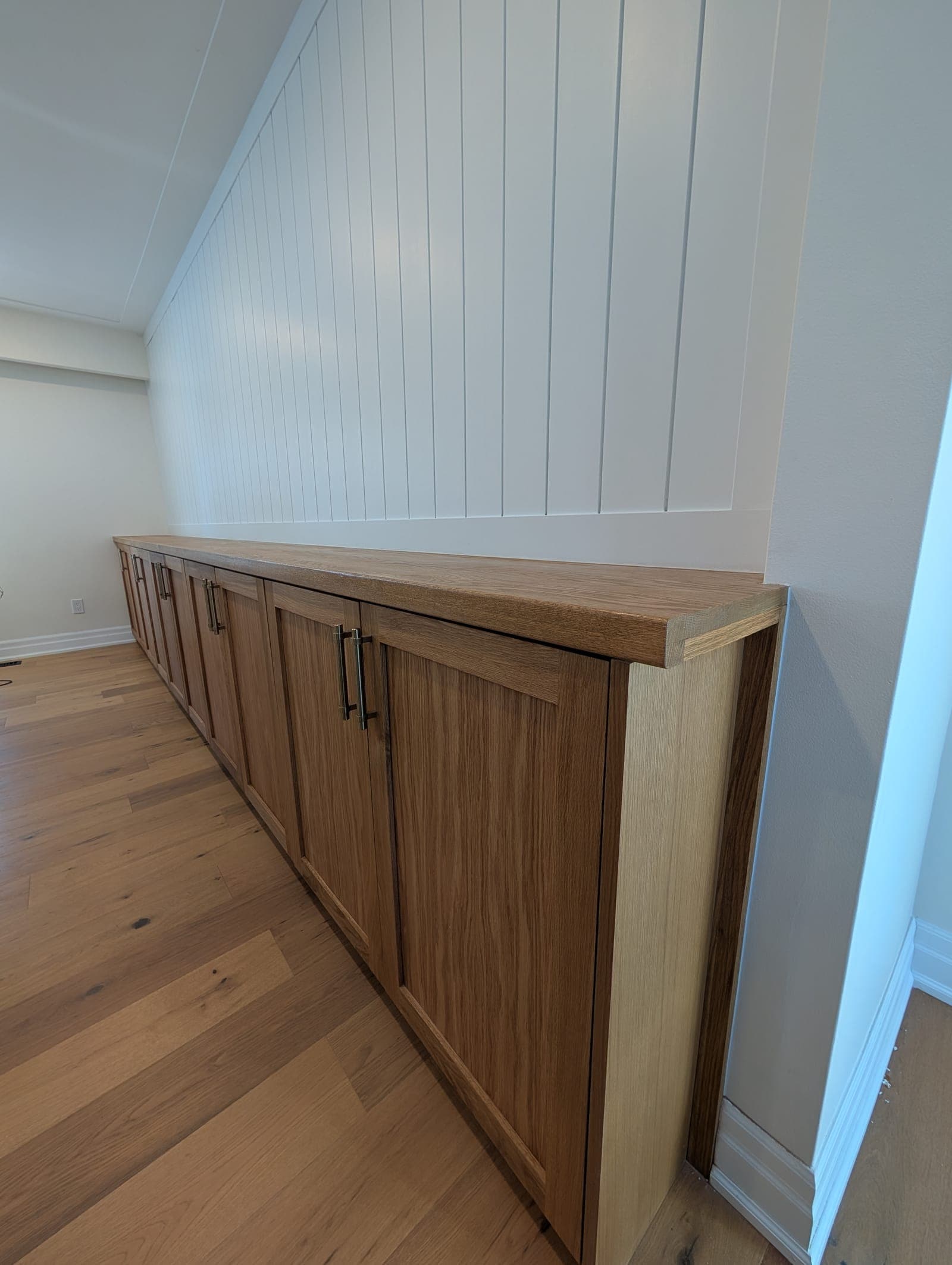 Long run of white oak base cabinets with a matching solid wood top beneath a white shiplap wall