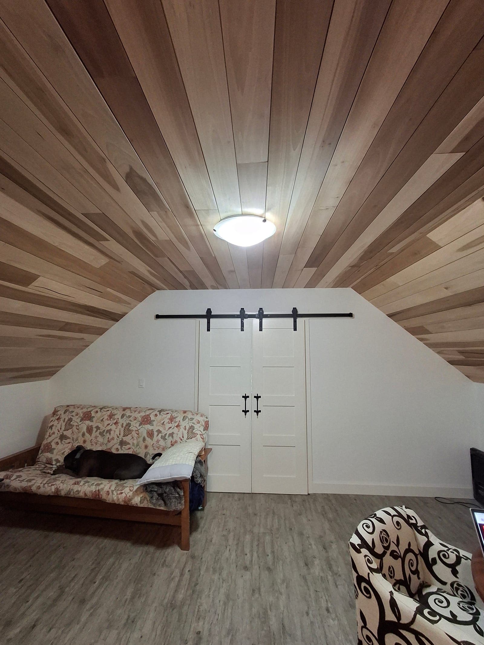 Attic living space with a cedar-plank vaulted ceiling and white sliding barn doors on black rail hardware