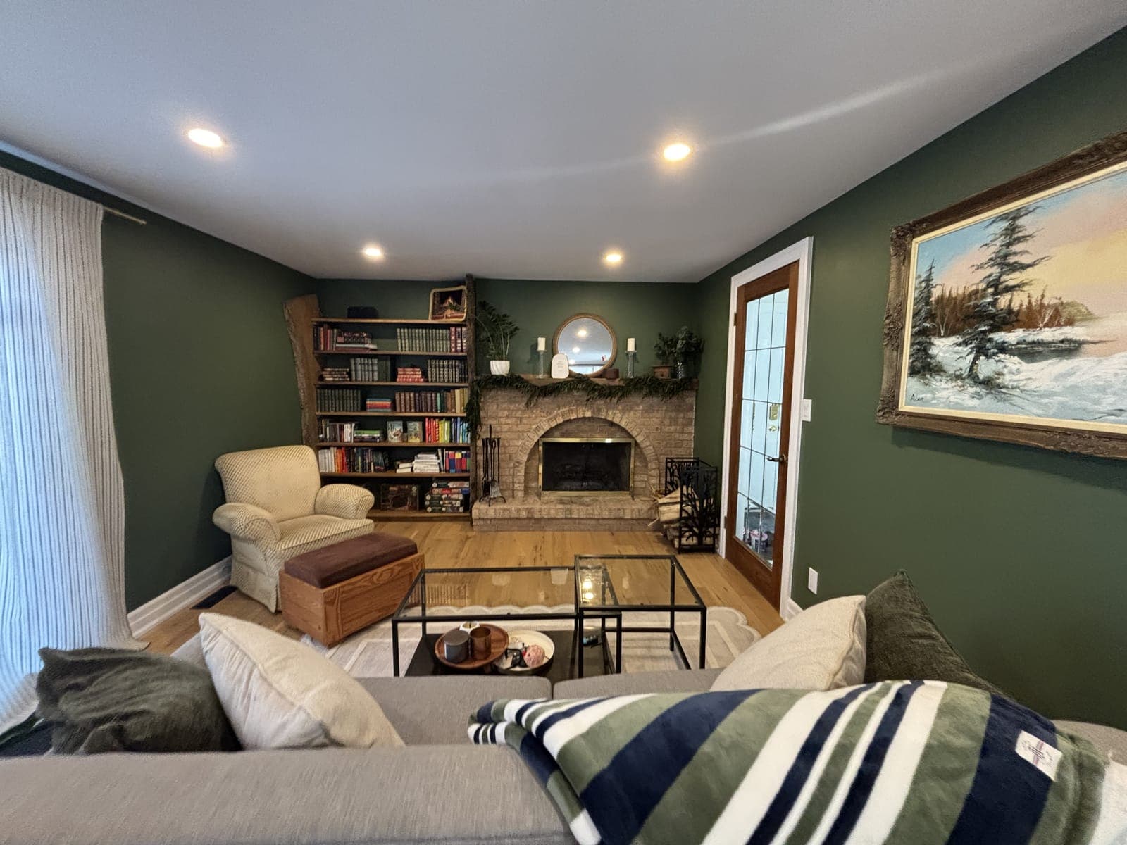 Family room with deep green walls, a brick fireplace, built-in bookshelves, and oak flooring