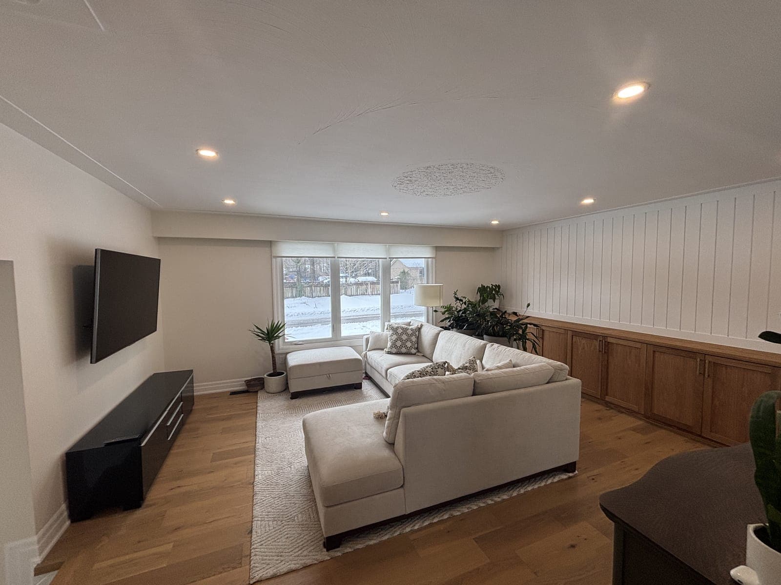 Living room with a white shiplap wall, a long oak built-in cabinet run, wall-mounted television, and oak flooring